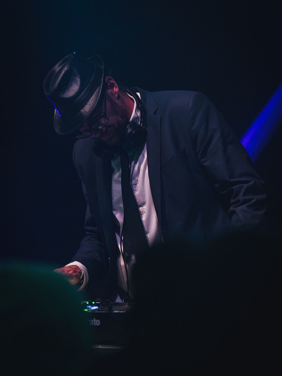Julien Bonhomme penché sur son contrôleur, chapeau sur les yeux et casque autour du cou, dans une pénombre bleu nuit.