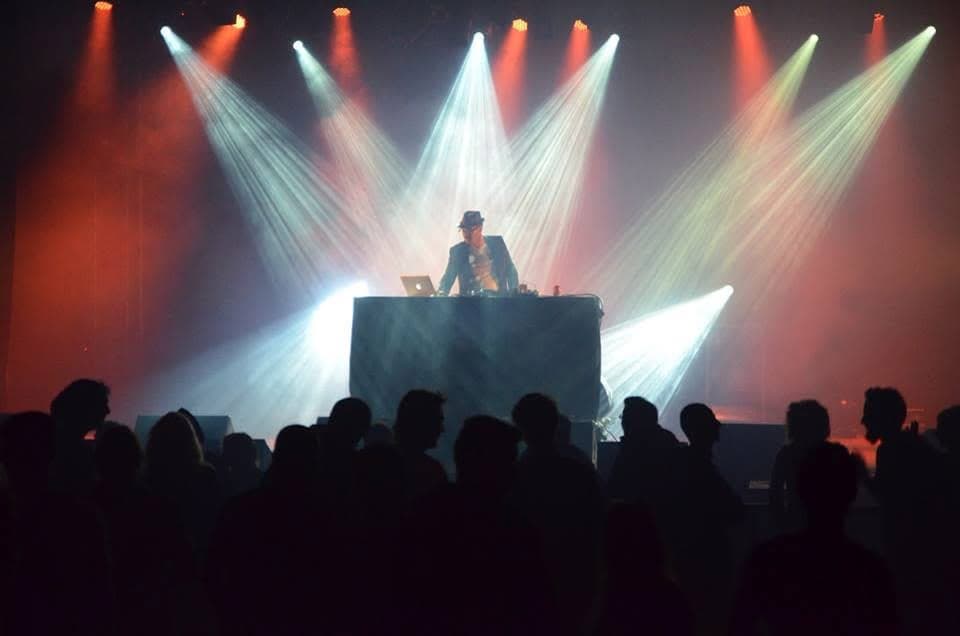 Plan large d'une salle de concert, Julien Bonhomme en silhouette derrière sa console, public de dos.